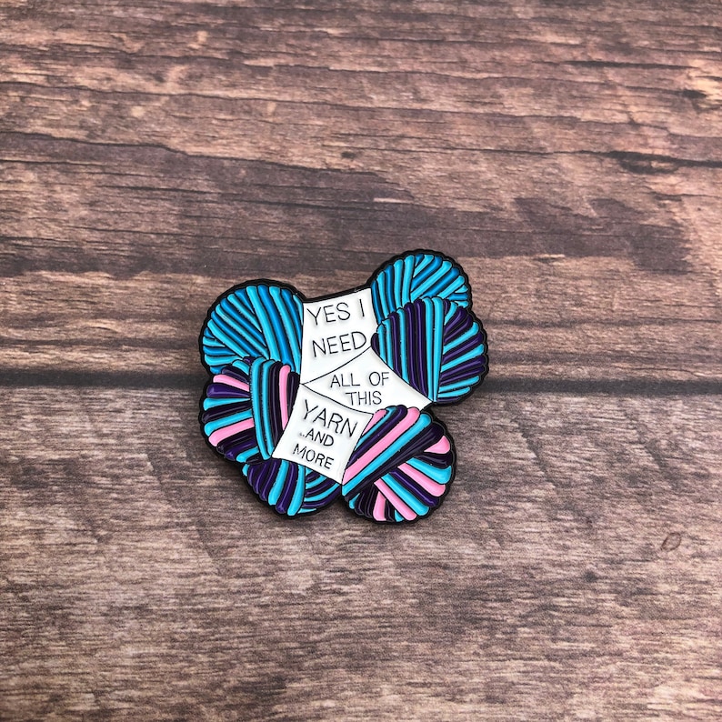 May include: A colorful enamel pin featuring a pile of yarn with the text "Yes I need all of this yarn...and more".