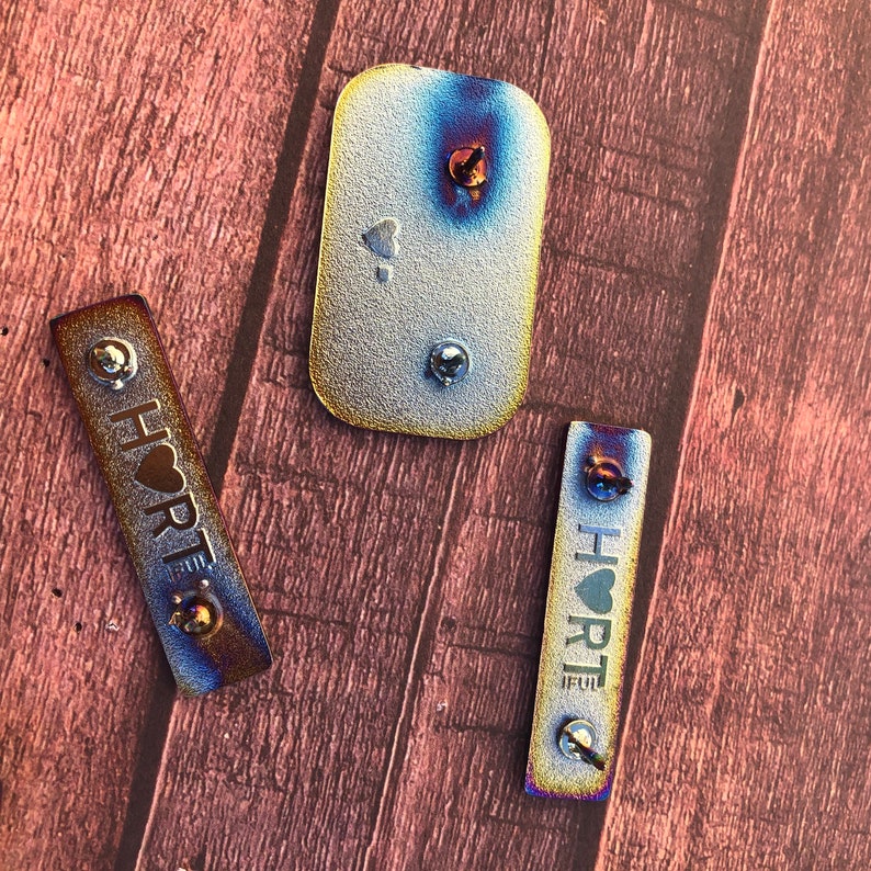 Peut inclure: Trois &eacute;tiquettes m&eacute;talliques avec un motif de c&oelig;ur et le mot "HEART" sur deux des &eacute;tiquettes. Les &eacute;tiquettes sont de couleur argent&eacute;e avec un reflet arc-en-ciel iridescent.