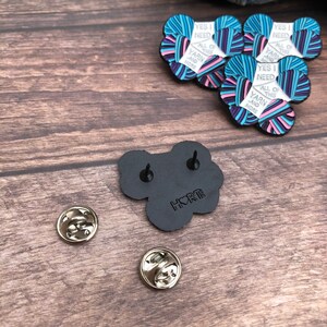 May include: A black enamel pin with a yarn ball design. The pin says "Yes I need all of this yarn and more". The back of the pin has a black backing with the word "HORT" in white.
