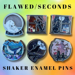Op de afbeelding: Een verzameling shaker emaille pins met diverse ontwerpen. De pins tonen afbeeldingen van een ijsberen familie, een kat bij een raam, een walvis, een wolf die naar de maan huilt en katten onder kersenbloesems. De tekst "FLAWED/SECONDS" en "SHAKER ENAMEL PINS" worden weergegeven.
