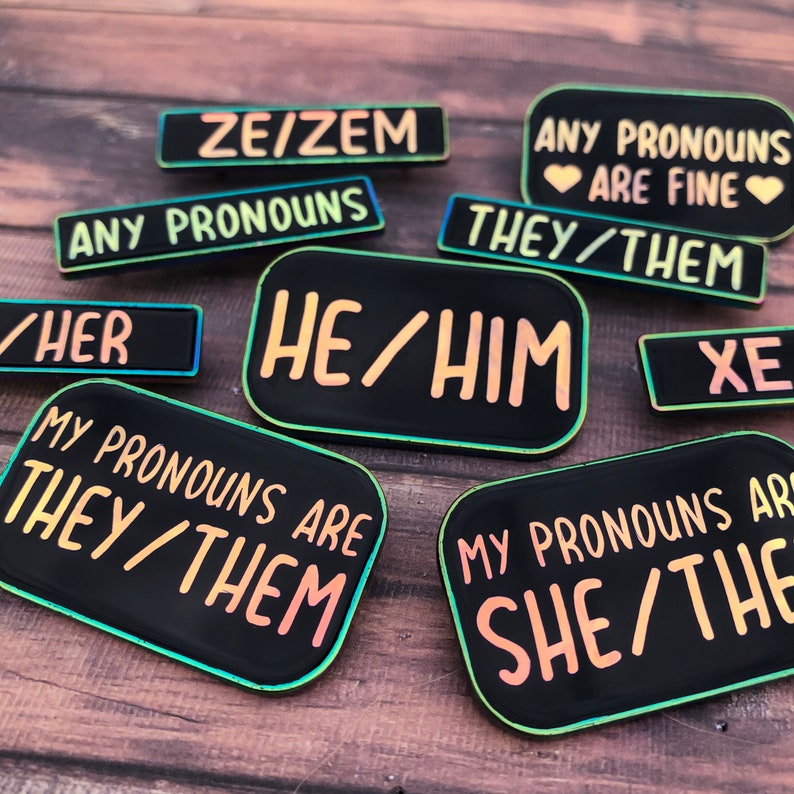Peut inclure: Un ensemble de huit &eacute;pingles en &eacute;mail noir avec des bordures arc-en-ciel iris&eacute;es. Les &eacute;pingles pr&eacute;sentent diff&eacute;rentes combinaisons de pronoms, notamment "ZE/ZEM", "ANY PRONOUNS ARE FINE", "THEY/THEM", "HE/HIM", "SHE/THE", "MY PRONOUNS ARE THEY/THEM", "MY PRONOUNS ARE SHE/THE", et "XE".