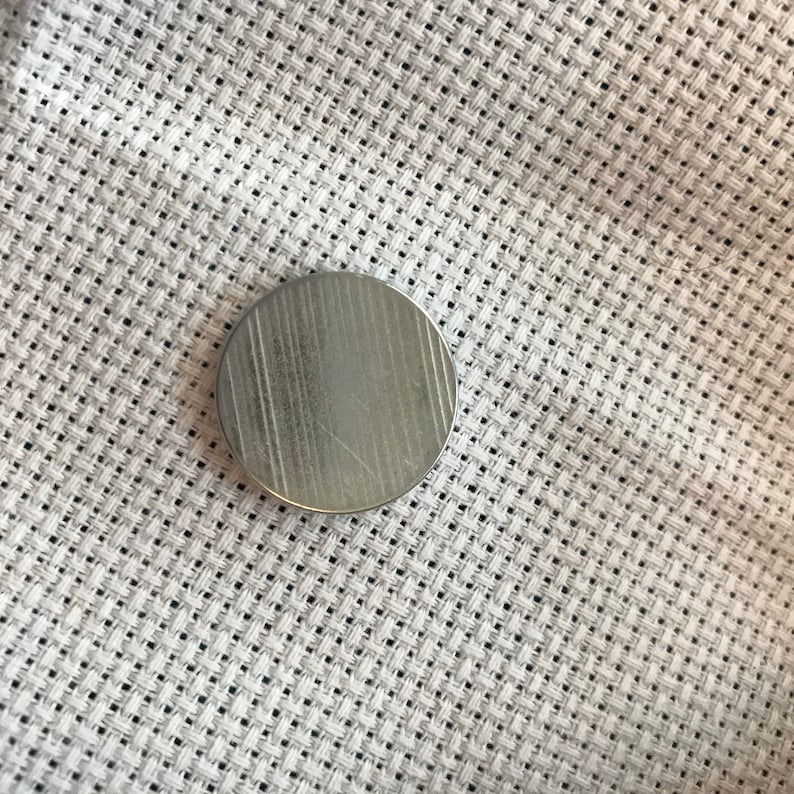 May include: A silver-colored metal disc with a textured surface.