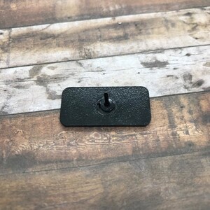 K&ouml;nnte beinhalten: Eine rechteckige schwarze Kunststoff-Schalterplatte mit einem einzigen Schraubenloch in der Mitte.