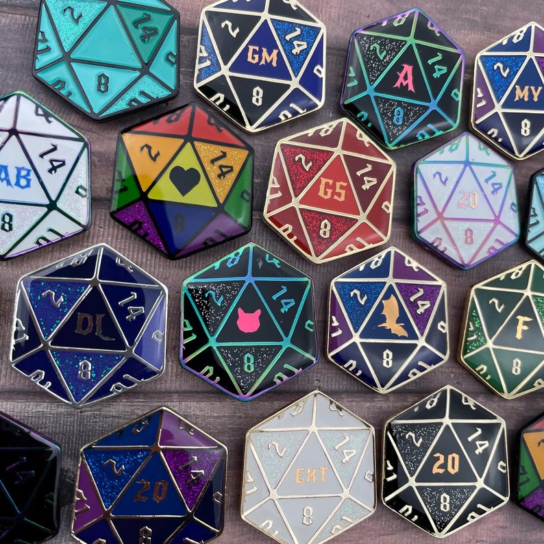 May include: A collection of 14 colorful enamel pins shaped like 20-sided dice. Each die has a different design and color scheme, including a black and green die with a cat, a red and gold die with the number 5, and a blue and silver die with the letter "DL".