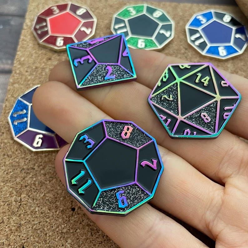 May include: A set of iridescent enamel pins shaped like dice with glitter accents. The dice are numbered 2, 3, 6, 8, 11, and 14.