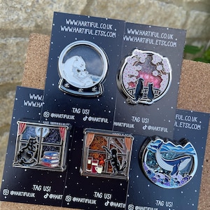 Puede incluir: Una colecci&oacute;n de pines esmaltados con varios dise&ntilde;os. Un pin representa un oso polar y su cachorro en una bola de nieve. Otros pines muestran gatos, flores de cerezo y una ballena. Cada pin est&aacute; en una tarjeta negra con informaci&oacute;n de sitio web y redes sociales.