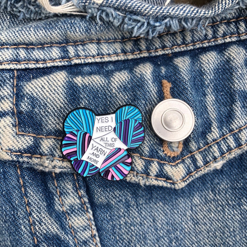May include: A white enamel pin with a colorful yarn design. The pin says "Yes I need all of this yarn and more".