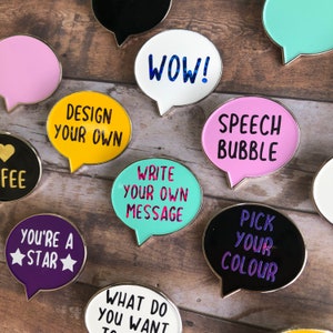 May include: Assortment of colorful enamel pins shaped like speech bubbles. The pins feature various phrases, including "WOW!" "Design your own", "Write your own message", "Speech Bubble", "Pick your color", and "You're a star".