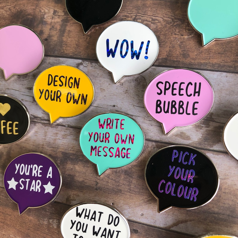 May include: Assortment of colorful enamel pins shaped like speech bubbles. The pins feature various phrases, including "WOW!" "Design your own", "Write your own message", "Speech Bubble", "Pick your color", and "You're a star".