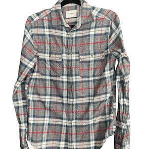 May include: A gray, blue, red, and white plaid button-down shirt with two chest pockets. The shirt is hanging on a black hanger. The brand name "Goodfellow" is visible on the collar.