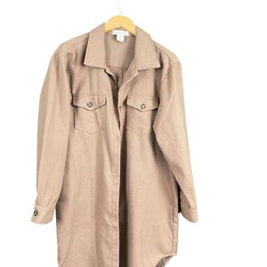 May include: A long-sleeved, light brown button-down shirt with two flap pockets and a curved hem.