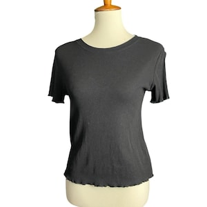 May include: A black, short-sleeved, ribbed knit top with a round neckline and a scalloped hem. The shirt is displayed on a mannequin. The fabric has vertical ribbing.