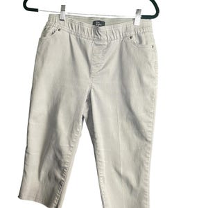 May include: Light beige capri pants with an elastic waistband and pockets, hanging on a black hanger. The pants have a straight leg and are made of a soft, durable fabric. The brand name "Kim Karen" is visible on the waistband.
