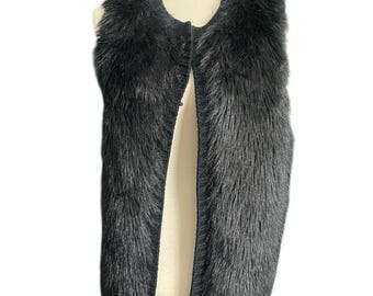 May include: A black faux fur vest displayed on a mannequin. The vest has a round neckline and a button closure. The faux fur is long and shaggy, giving the vest a textured appearance. The vest is sleeveless and appears to be a medium size.