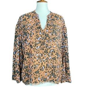 May include: A long-sleeved blouse with a V-neck and a unique animal print pattern. The blouse features a combination of brown, black, and light purple spots on a peach-colored background. The bottom hem has a fringed edge.