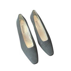 Puede incluir: Un par de zapatos de salón de ante negro con punta puntiaguda y tacón bajo. Los zapatos están etiquetados con "Calico" en el interior.