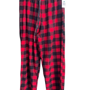 May include: Red and black plaid pajama pants with a drawstring waist and a zipper fly. The pants are hanging on a black hanger against a white background. A price tag is attached to the pants.