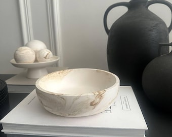 May include: A white marble bowl with brown marbling. The bowl is sitting on a stack of books with a white cover. The text "The Poetry Company" is visible on the book cover.