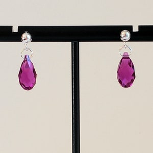 Könnte beinhalten: Ein Paar silberne Ohrstecker mit einem tropfenförmigen, facettierten, fuchsia-farbenen Kristall, der an jedem Ohrring hängt.