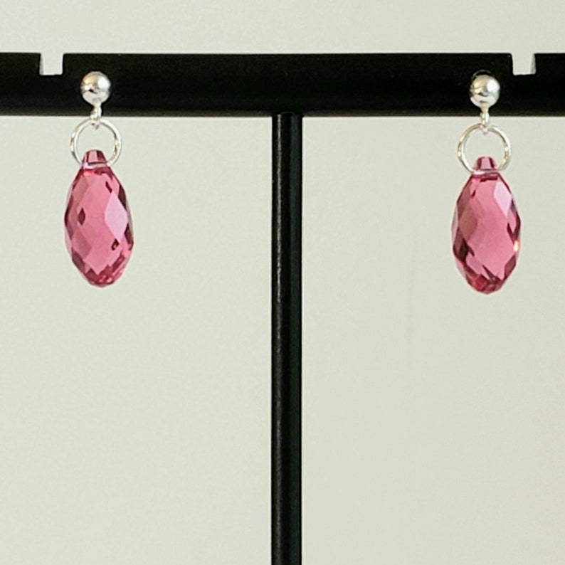 May include: A pair of silver stud earrings with pink faceted teardrop-shaped crystals.