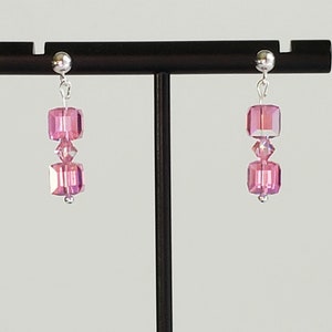 May include: A pair of silver earrings with pink crystal beads. The earrings are hanging from a black stand.