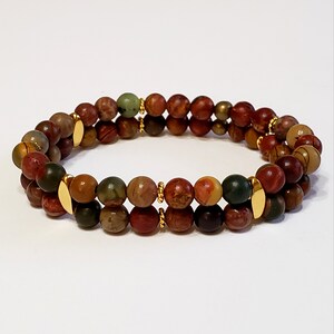 May include: A double-strand bracelet made with brown, red, and green jasper beads and gold accents.