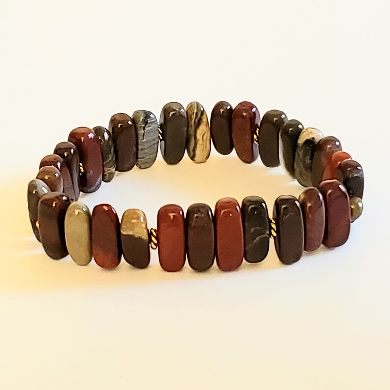May include: A red, brown, and beige stone bracelet with gold accents. The bracelet is made of multiple oval-shaped stones.
