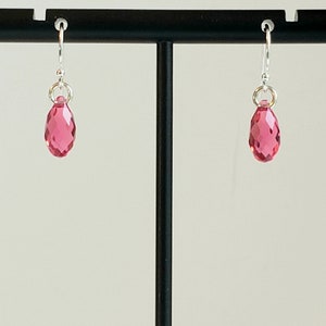 May include: A pair of silver earrings with pink teardrop-shaped crystals.