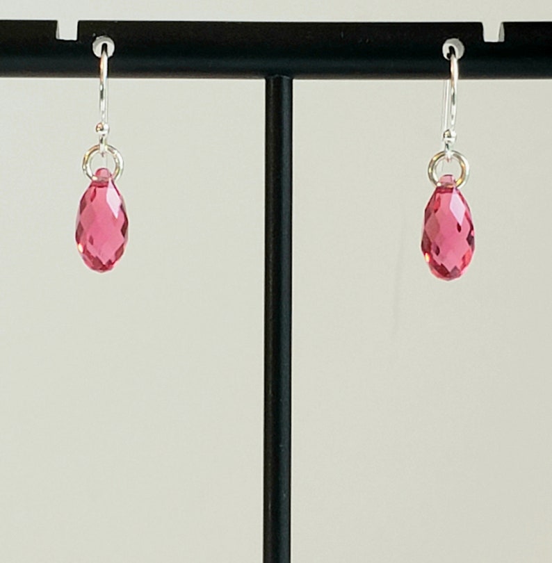 May include: A pair of silver earrings with pink teardrop-shaped crystals.