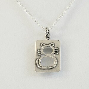 May include: A silver necklace with a rectangular pendant featuring a cutout design of a cat. The pendant has a smooth, polished finish.