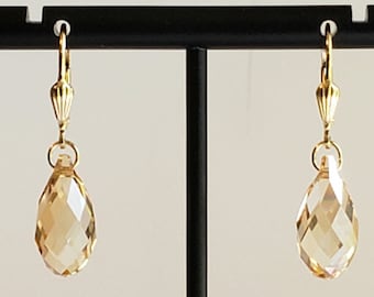 May include: A pair of gold-toned leverback earrings featuring faceted, teardrop-shaped champagne-colored crystals. The crystals are suspended from a ribbed gold-toned metal finding, creating a clear, reflective, and symmetrical drop earring design.