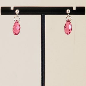 May include: A pair of silver stud earrings with pink teardrop-shaped crystals hanging from them.