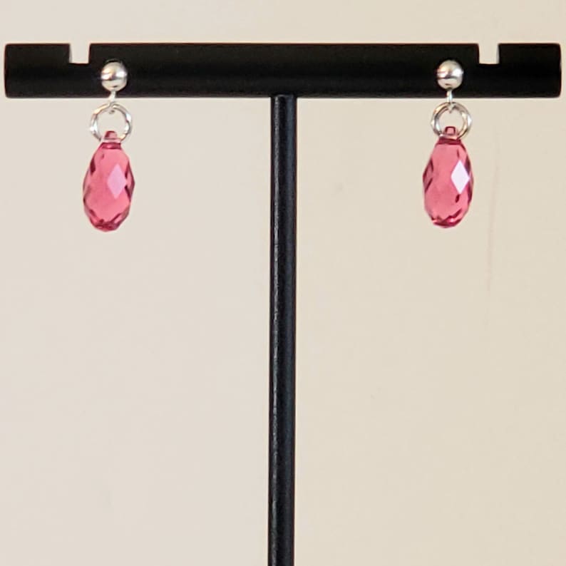 May include: A pair of silver stud earrings with pink teardrop-shaped crystals hanging from them.