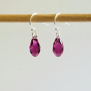 May include: A pair of silver dangle earrings with teardrop-shaped pink crystal stones.