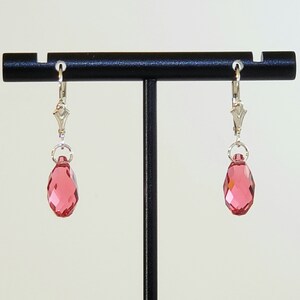 May include: A pair of silver dangle earrings with pink teardrop-shaped crystals.