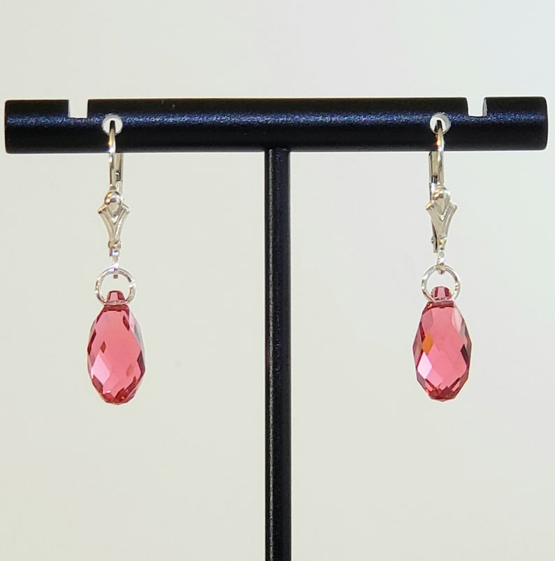 May include: A pair of silver dangle earrings with pink teardrop-shaped crystals.