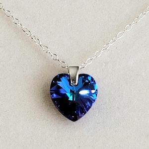 May include: A heart-shaped pendant necklace with a vibrant blue crystal. The pendant hangs from a delicate silver chain. The crystal has multiple facets, creating a sparkling effect. The necklace is displayed against a light background.