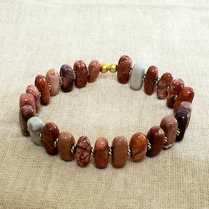 May include: A bracelet made of brown, red, and white stones with gold accents. The stones are oval shaped and are strung together with wire.