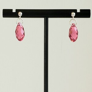 May include: A pair of silver stud earrings with pink crystal teardrop dangles.