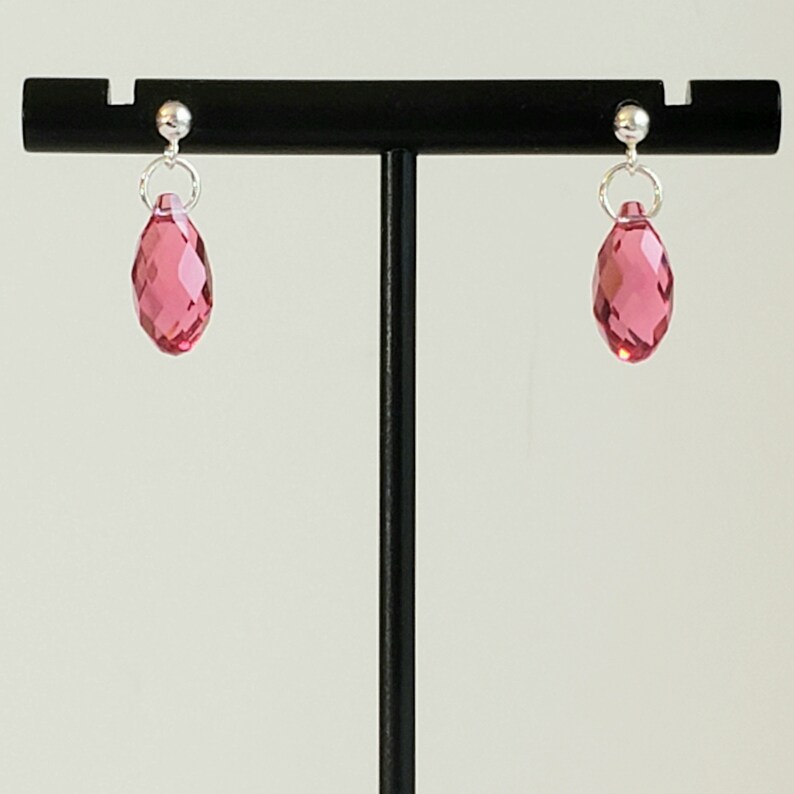 May include: A pair of silver stud earrings with pink crystal teardrop dangles.