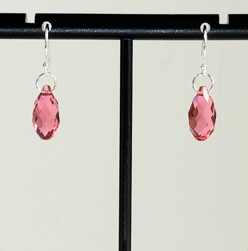 May include: A pair of silver earrings with pink crystal teardrop dangles.
