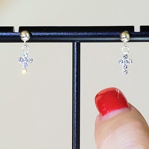 May include: A pair of silver dangle earrings with a small cross charm adorned with clear cubic zirconia stones.