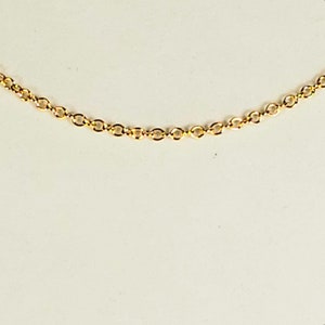 May include: A delicate gold-colored chain necklace with small, oval-shaped links. The chain is displayed against a plain, off-white background, highlighting its simple elegance. The necklace is a fine piece of jewelry.