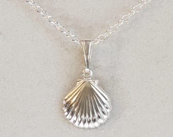 May include: A silver-toned necklace featuring a pendant shaped like a scallop shell. The pendant is suspended from a delicate silver-toned chain with oval links. The shell design has vertical ridges and a polished, reflective metallic finish.