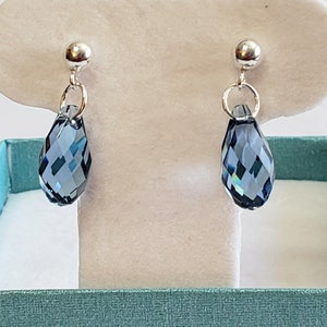 May include: A pair of elegant drop earrings. Each earring features a faceted, teardrop-shaped, dark blue crystal pendant suspended from a silver-colored post. The earrings are displayed on a white background.