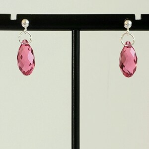 May include: A pair of silver stud earrings with pink faceted teardrop-shaped crystals.