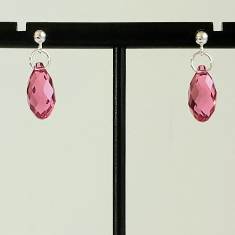 May include: A pair of silver stud earrings with pink faceted teardrop-shaped crystals.