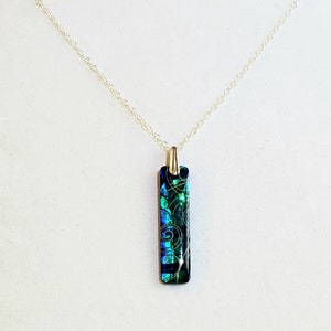 May include: A silver chain necklace with a rectangular pendant featuring a blue and green glass design with swirls of gold.