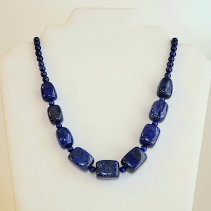 May include: A necklace made of dark blue lapis lazuli beads. The beads are rectangular and have a polished finish. The necklace is on a white mannequin.