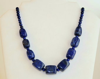May include: A necklace made of dark blue lapis lazuli beads. The beads are rectangular and have a polished finish. The necklace is on a white mannequin.